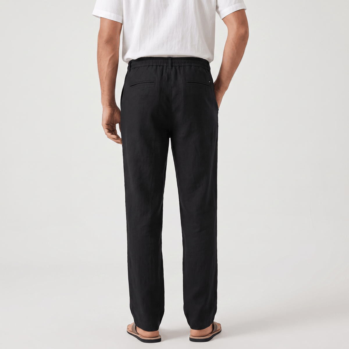Back view of men's black linen drawstring pants featuring an elastic waistband and relaxed fit.