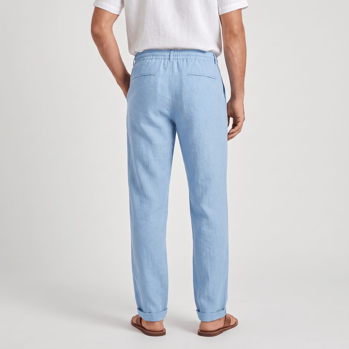 Back view of men's light blue linen drawstring pants with a relaxed silhouette and elastic waistband.