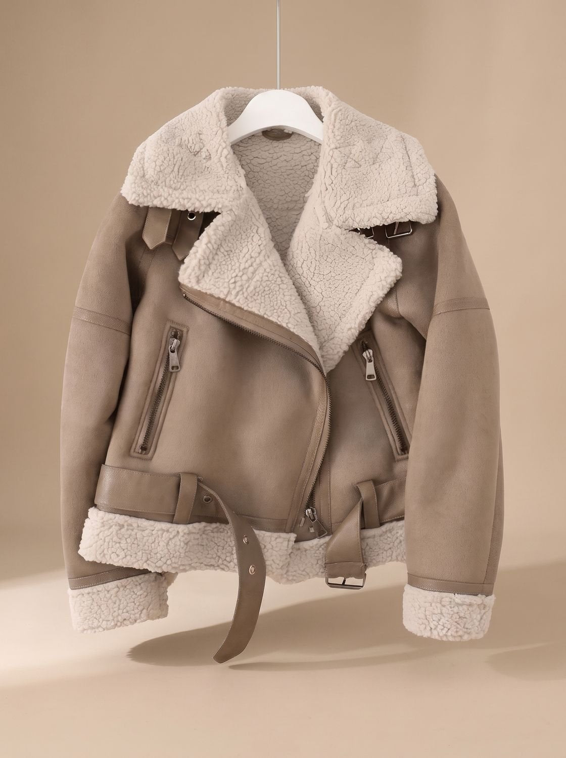 Taupe belted shearling aviator jacket for women shown on a hanger with asymmetrical zip and plush lining
