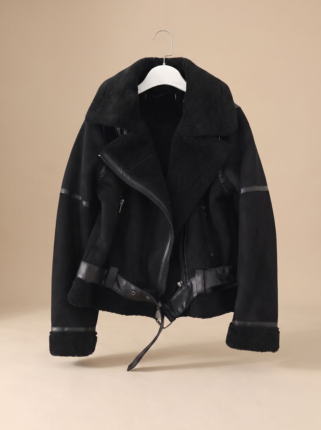 Black belted shearling aviator jacket for women shown on a hanger with asymmetrical zip and plush lining