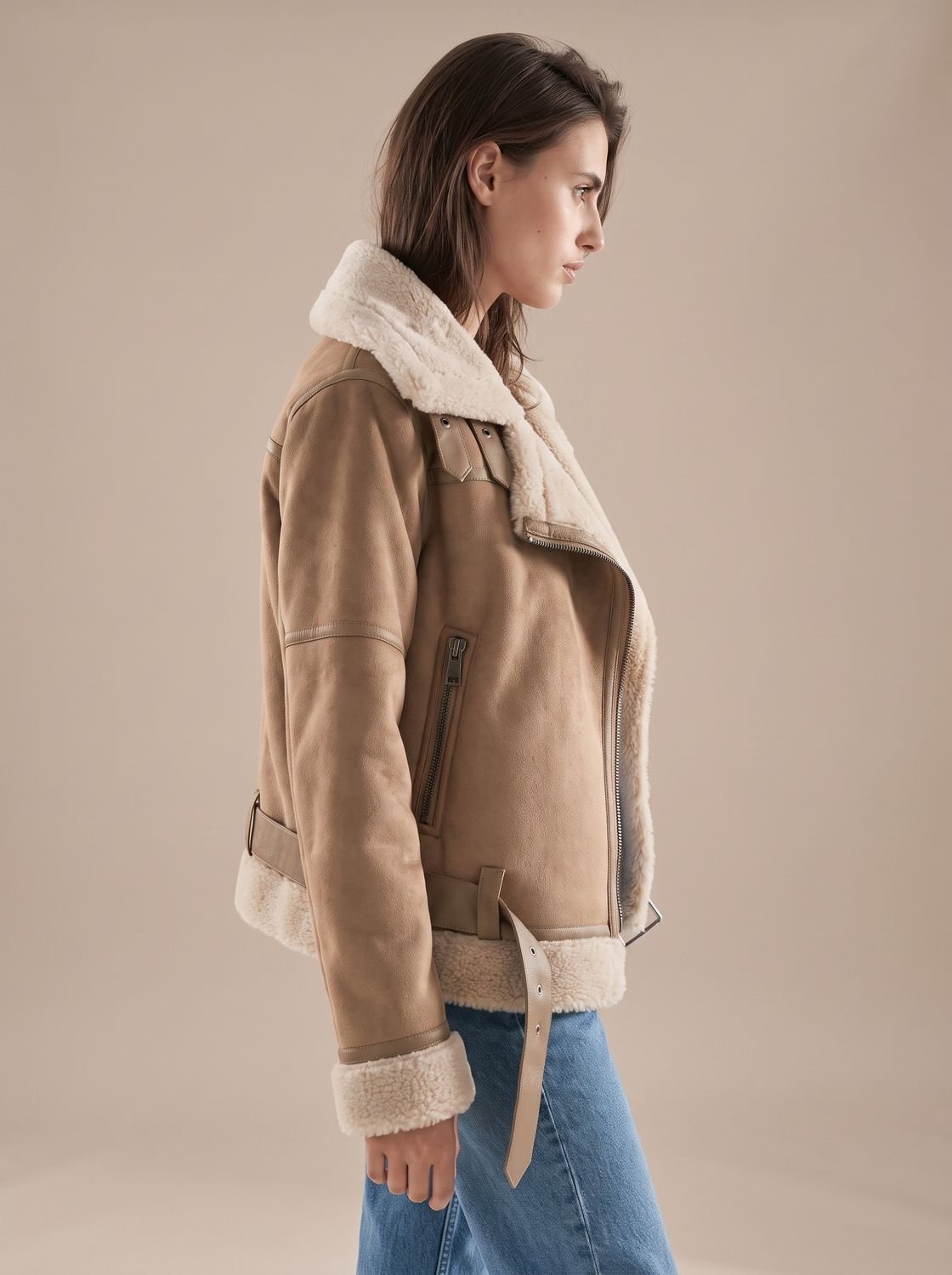 Taupe belted shearling aviator jacket worn by a woman, side view with asymmetrical zip and plush lining