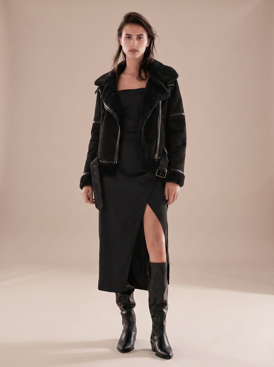 Black belted shearling aviator jacket worn by a woman with asymmetrical zip, plush lining, and wide collar