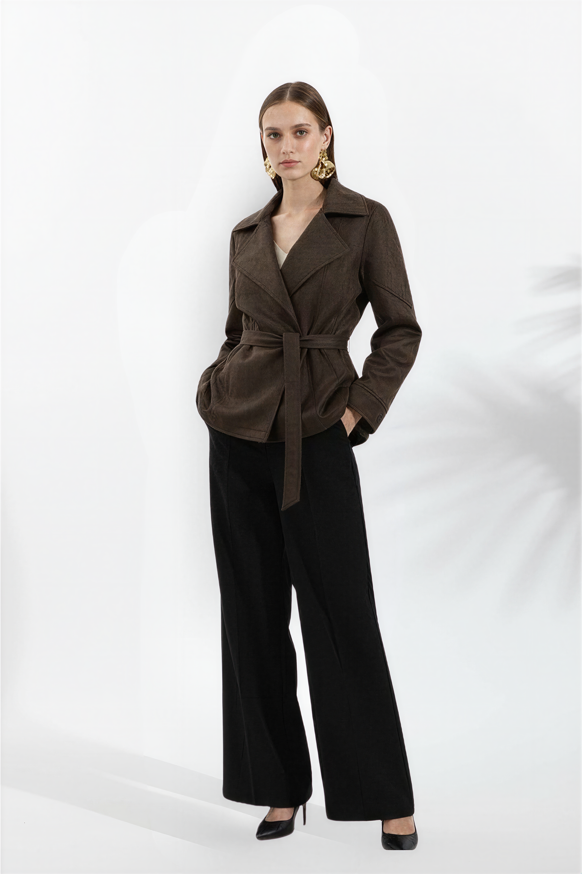 A woman wearing a dark brown belted suede jacket with a relaxed fit and turn-down collar, side view