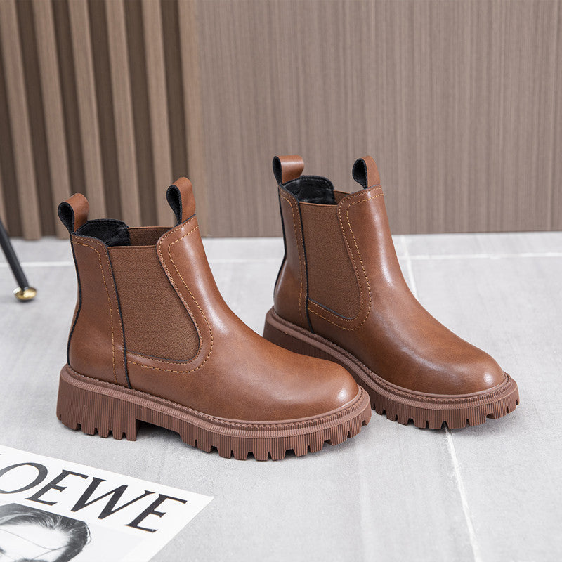 Pair of brown leather Chelsea boots for women with block heel and lug sole, styled on a tiled floor