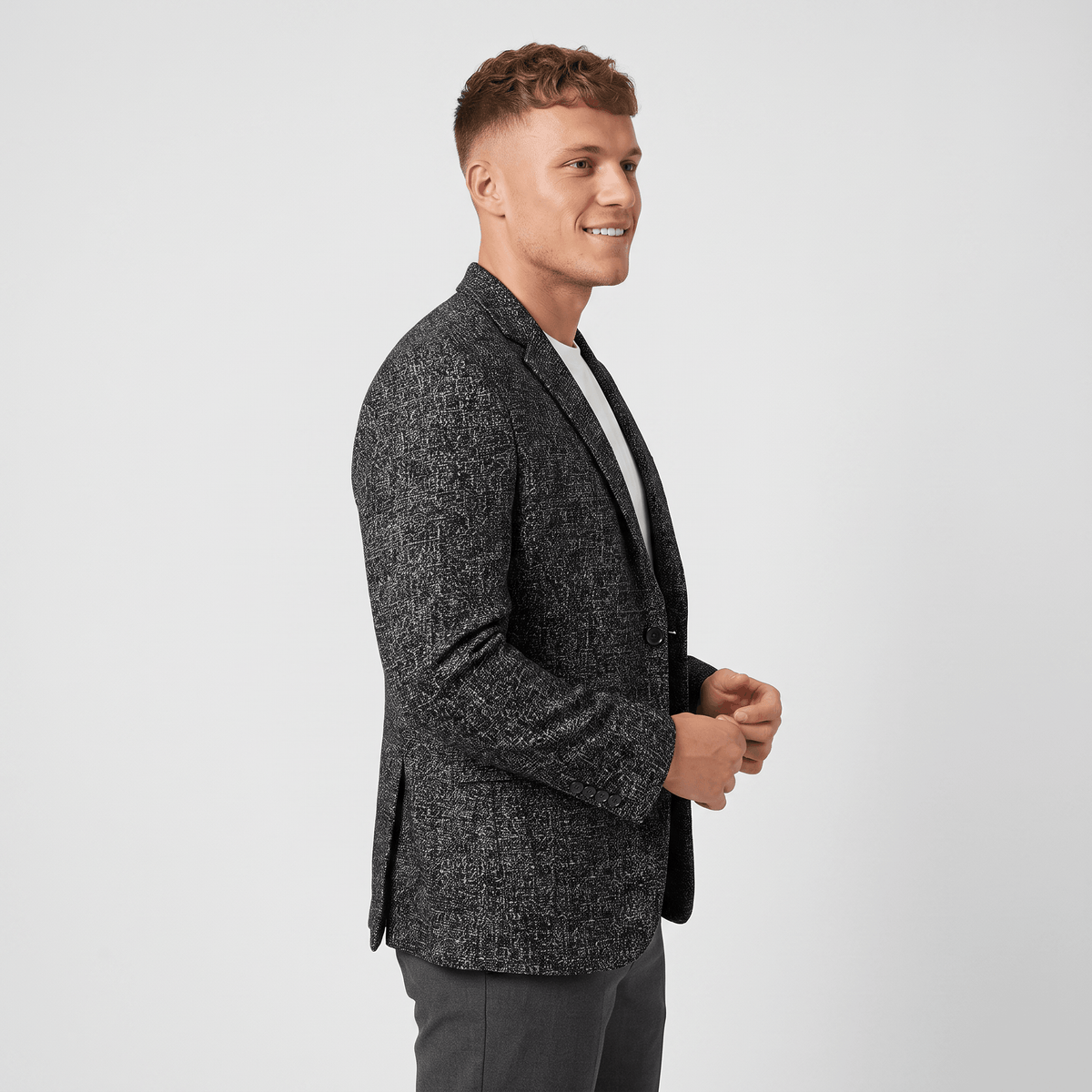 Side view of a man wearing a charcoal gray tweed blazer featuring a notched lapel, two-button closure, and tailored fit.