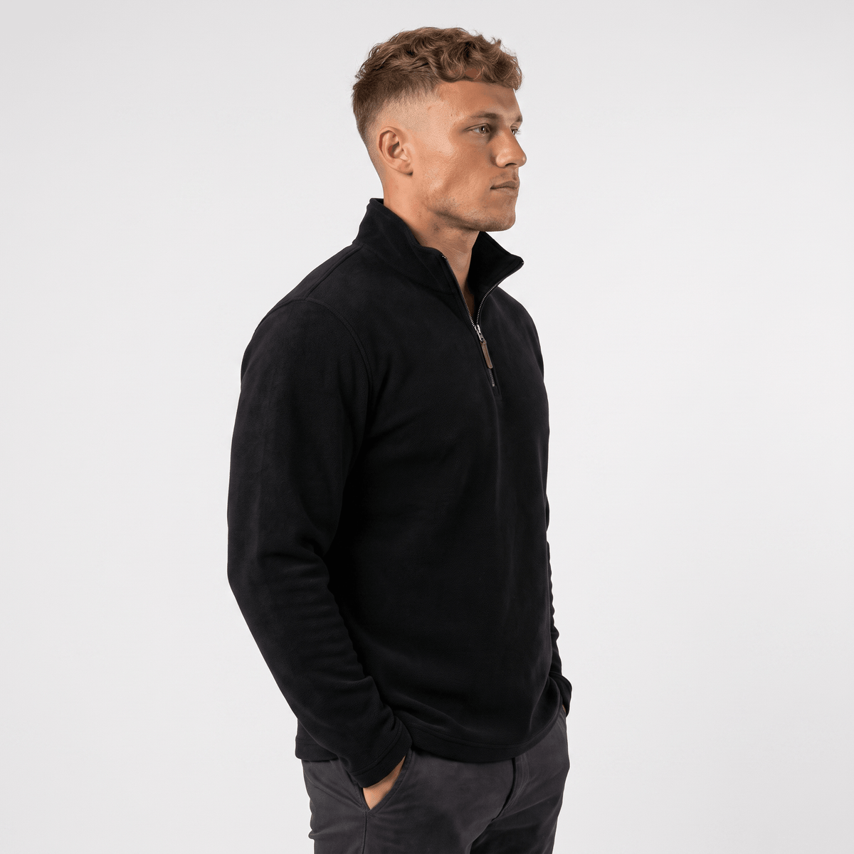 Side view of a man wearing a black quarter-zip sweater with a stand collar and classic silhouette.