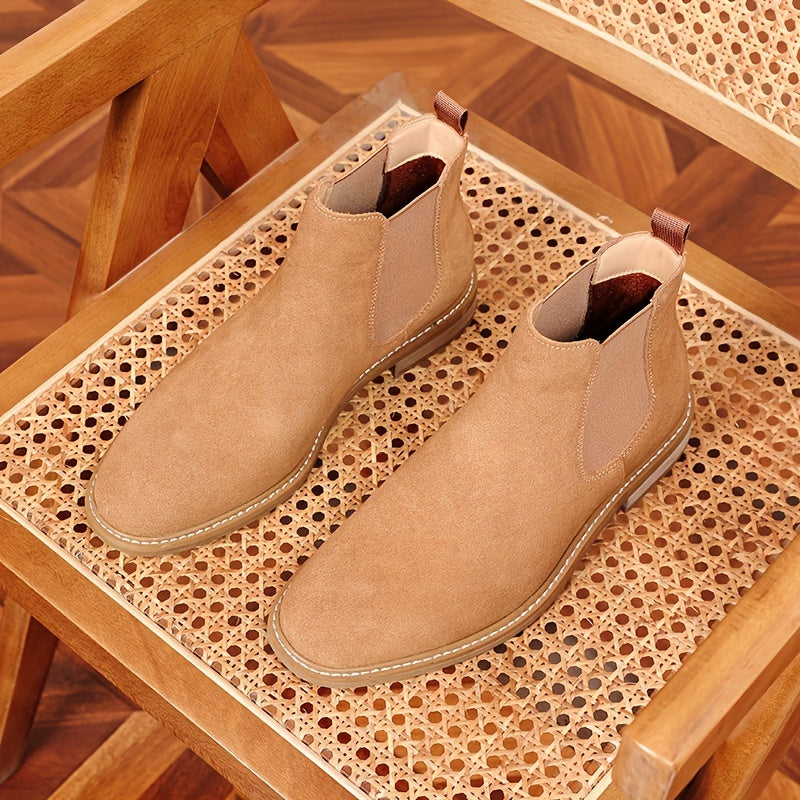 Tan suede Chelsea ankle boots for men seen from above on a cane chair seat, showing the rear pull tabs