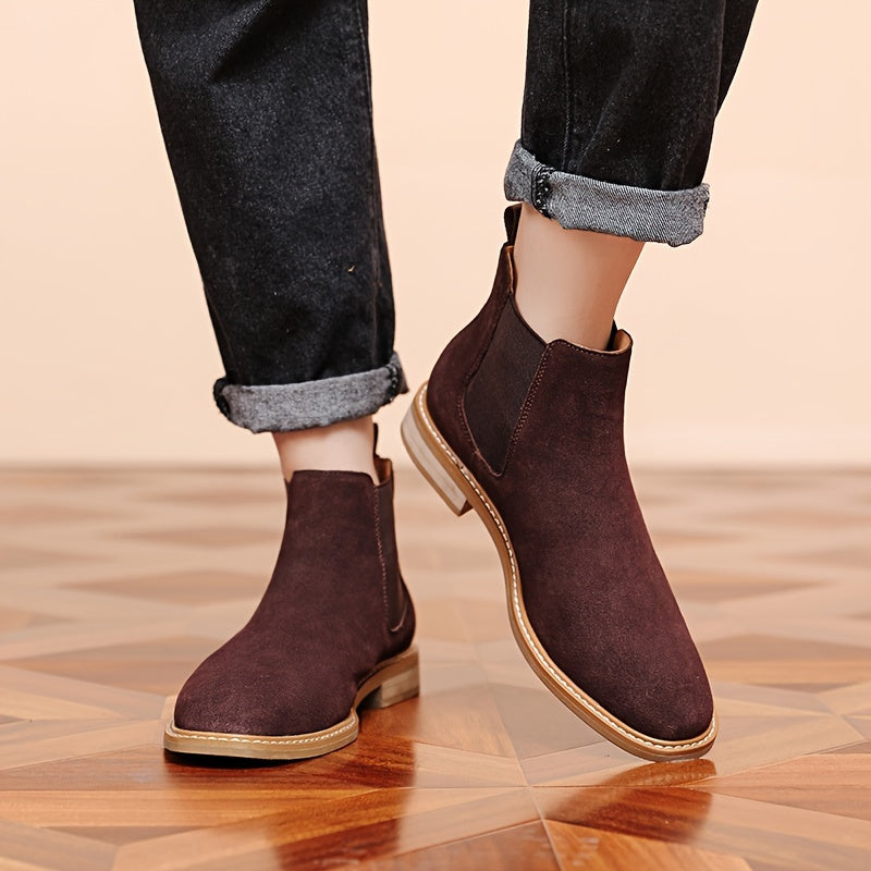 Man wearing dark brown Chelsea ankle boots with cuffed black jeans on a parquet floor