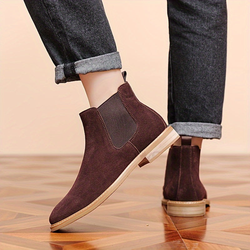 Dark brown Chelsea ankle boots worn with cuffed jeans, one foot raised to show the low stacked heel