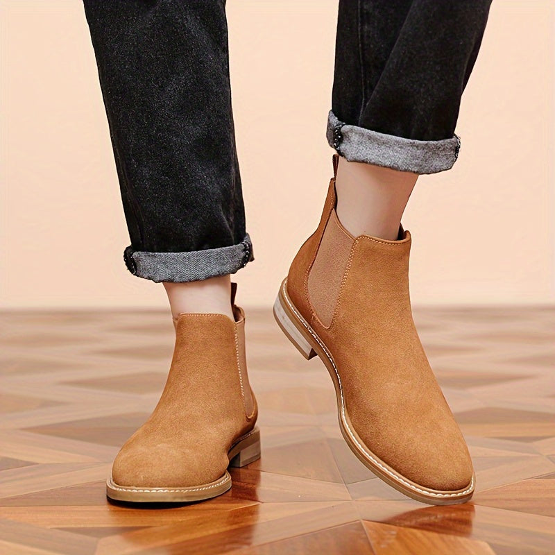 Man wearing tan suede Chelsea ankle boots with cuffed black jeans on a parquet floor