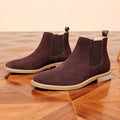 Pair of dark brown suede Chelsea ankle boots for men with pale contrast sole, on a parquet floor