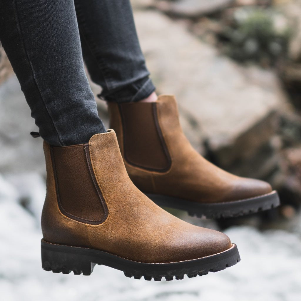 Brown chunky Chelsea boots for women with lug sole, worn with grey jeans outdoors