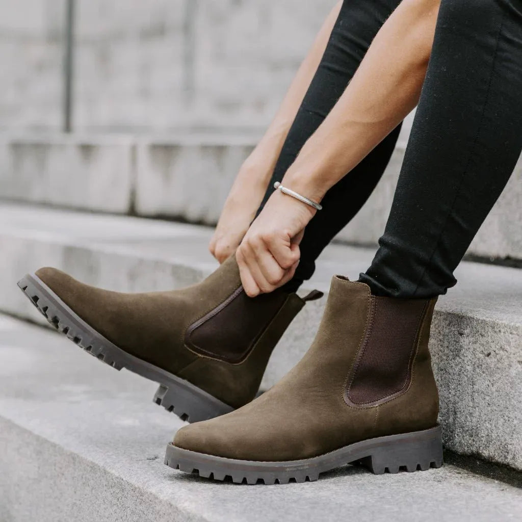 Woman adjusting dark green chunky Chelsea boots with lug sole, worn with black jeans on steps