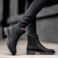 Black chunky Chelsea boots for women on a lug sole, worn with black jeans on a city pavement