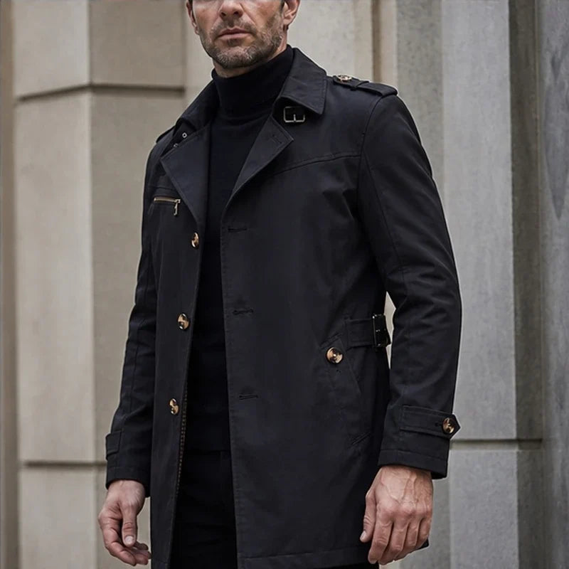 A man wearing a black cotton blend trench coat with a belted waist and double-breasted front