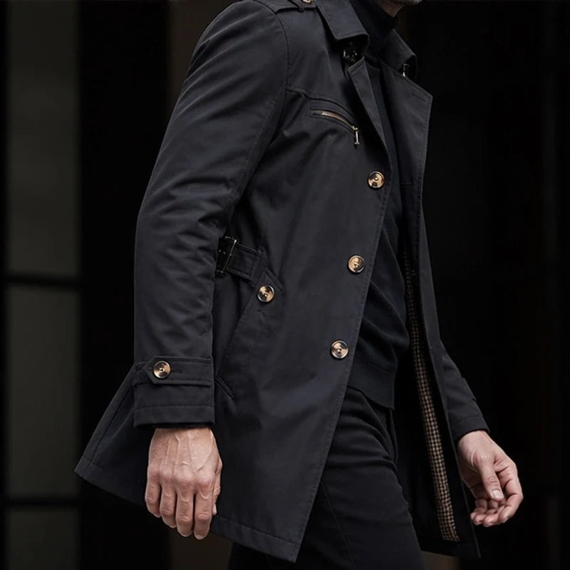 Close-up of a man wearing a black cotton blend trench coat, showing the double-breasted front, buttons, and belted waist