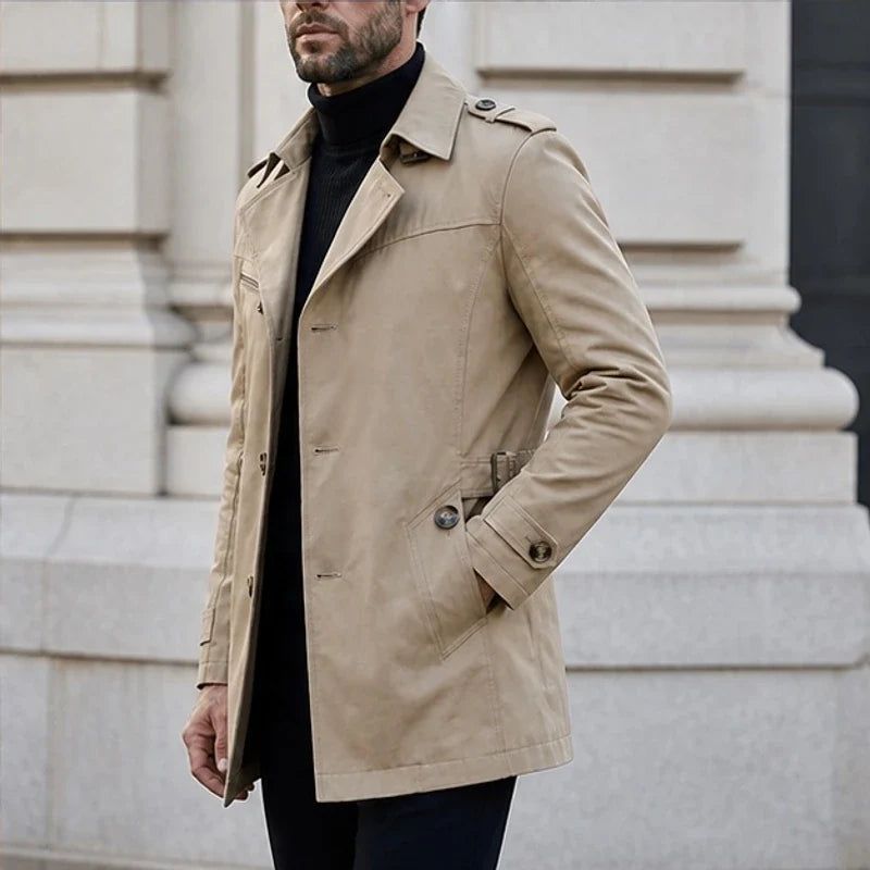 A man wearing a beige cotton blend trench coat with a belted waist, standing outdoors