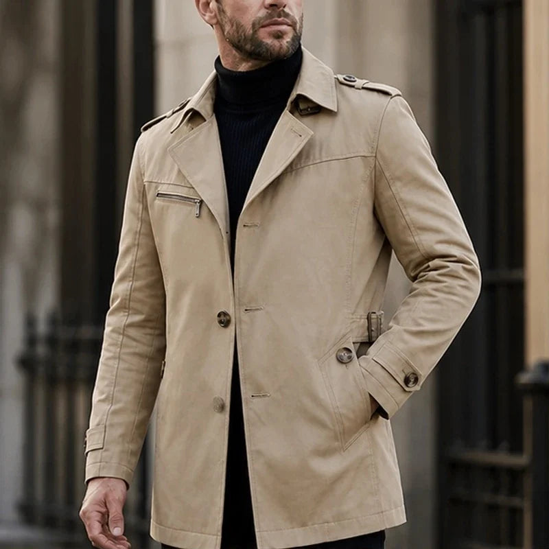 A man wearing a beige cotton blend trench coat with a belted waist and structured collar