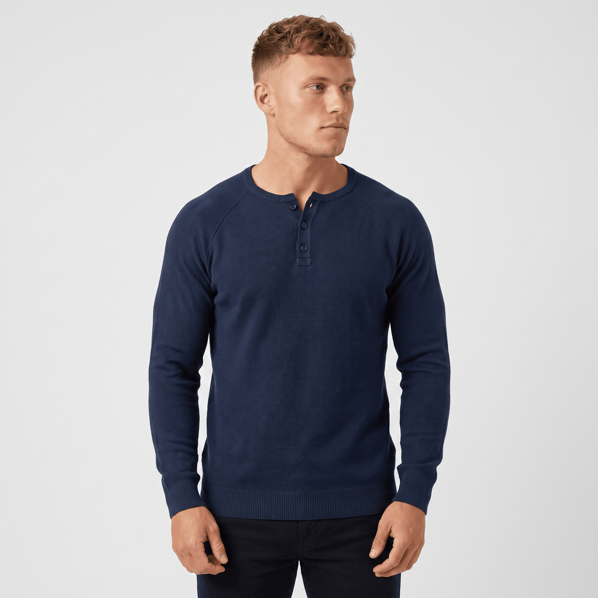 Man wearing a navy waffle knit Henley sweater with a three-button placket, long sleeves, and a modern slim fit.