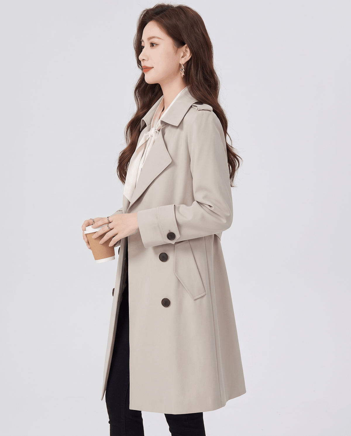 A woman wearing a cream double-breasted trench coat with a tailored fit and turn-down collar, shown in side view