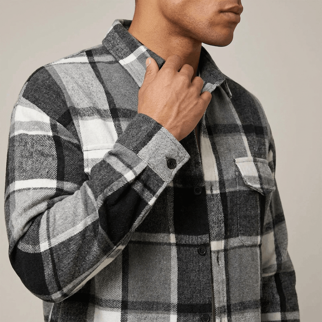 Close-up of a man wearing a black and white plaid overshirt jacket, showing the pointed collar, button closure, and textured plaid fabric.