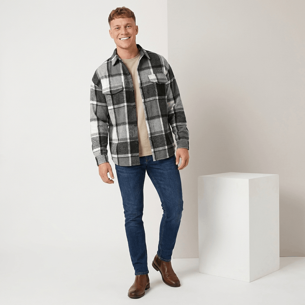 Man wearing a black and white plaid overshirt jacket with blue jeans and white sneakers in a studio setting.