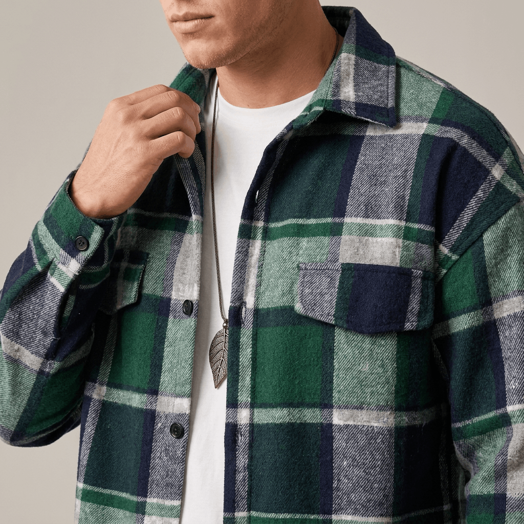Close-up of a man wearing a green, navy, and white plaid overshirt jacket with a button-front closure, pointed collar, and chest pocket.