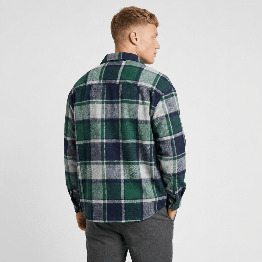 Back view of a man wearing a green, navy, and white plaid overshirt jacket with a relaxed fit and long sleeves.
