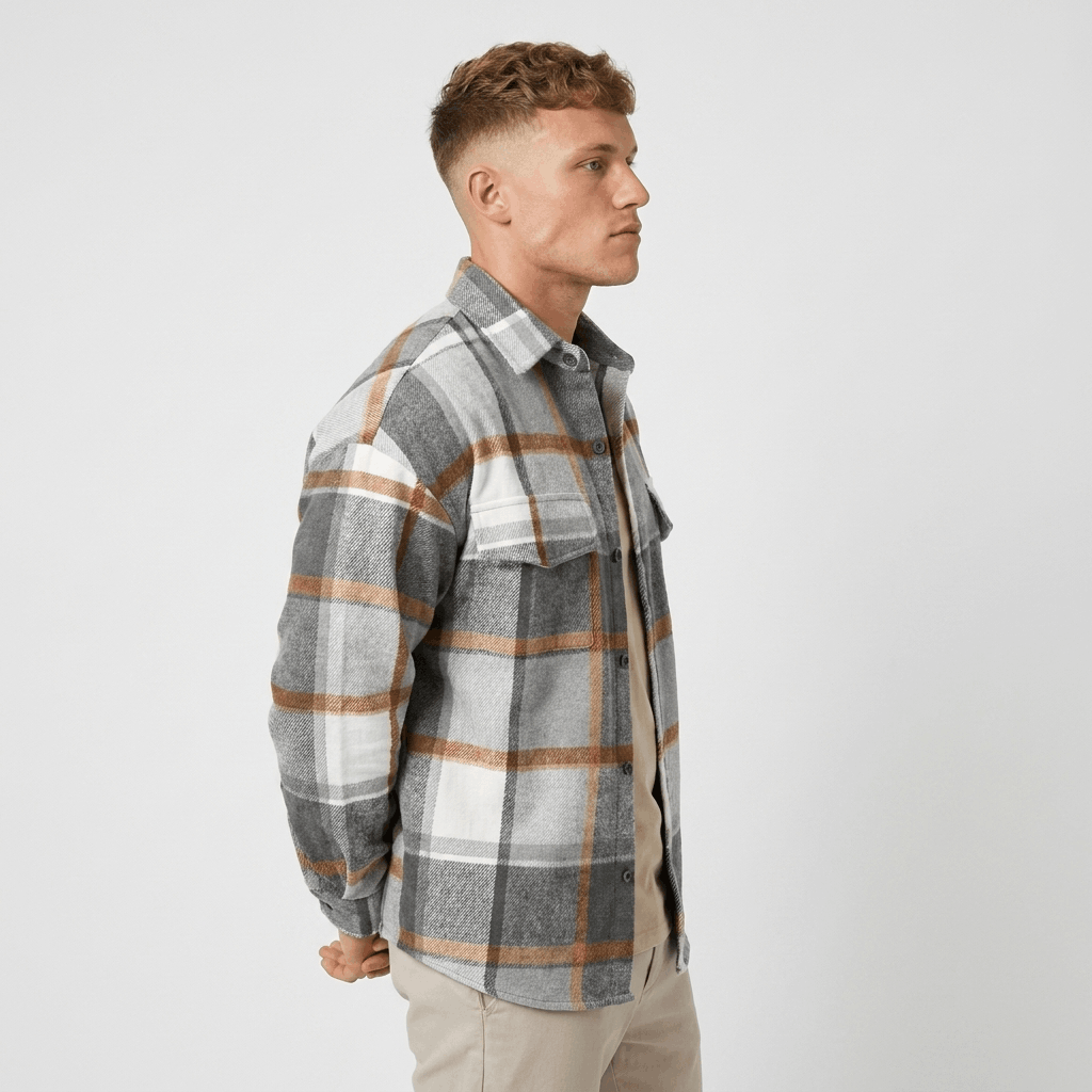 Side view of a man wearing a gray, white, and tan plaid overshirt jacket with a button-front closure, pointed collar, and chest pockets.