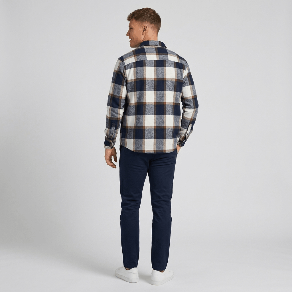 Man wearing a navy, gray, and cream plaid overshirt jacket with dark trousers, shown from the back in a full-body view.