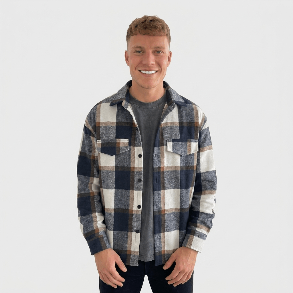 Man wearing a navy, gray, and cream plaid overshirt jacket with a button-front closure, pointed collar, chest pockets, and long sleeves over a dark gray shirt.