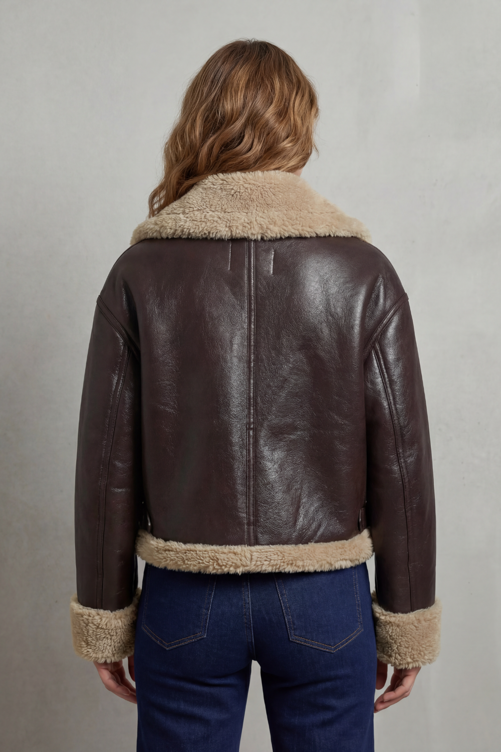A woman wearing a cropped fleece aviator jacket with a plush shearling collar and waistband, shown from the back
