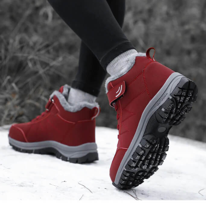 Red fleece-lined winter hiker boots with hook-and-loop straps and anti-slip soles, worn in snow