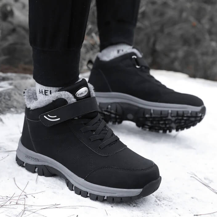 Black fleece-lined winter hiker boots with hook-and-loop straps and anti-slip soles, worn in snow
