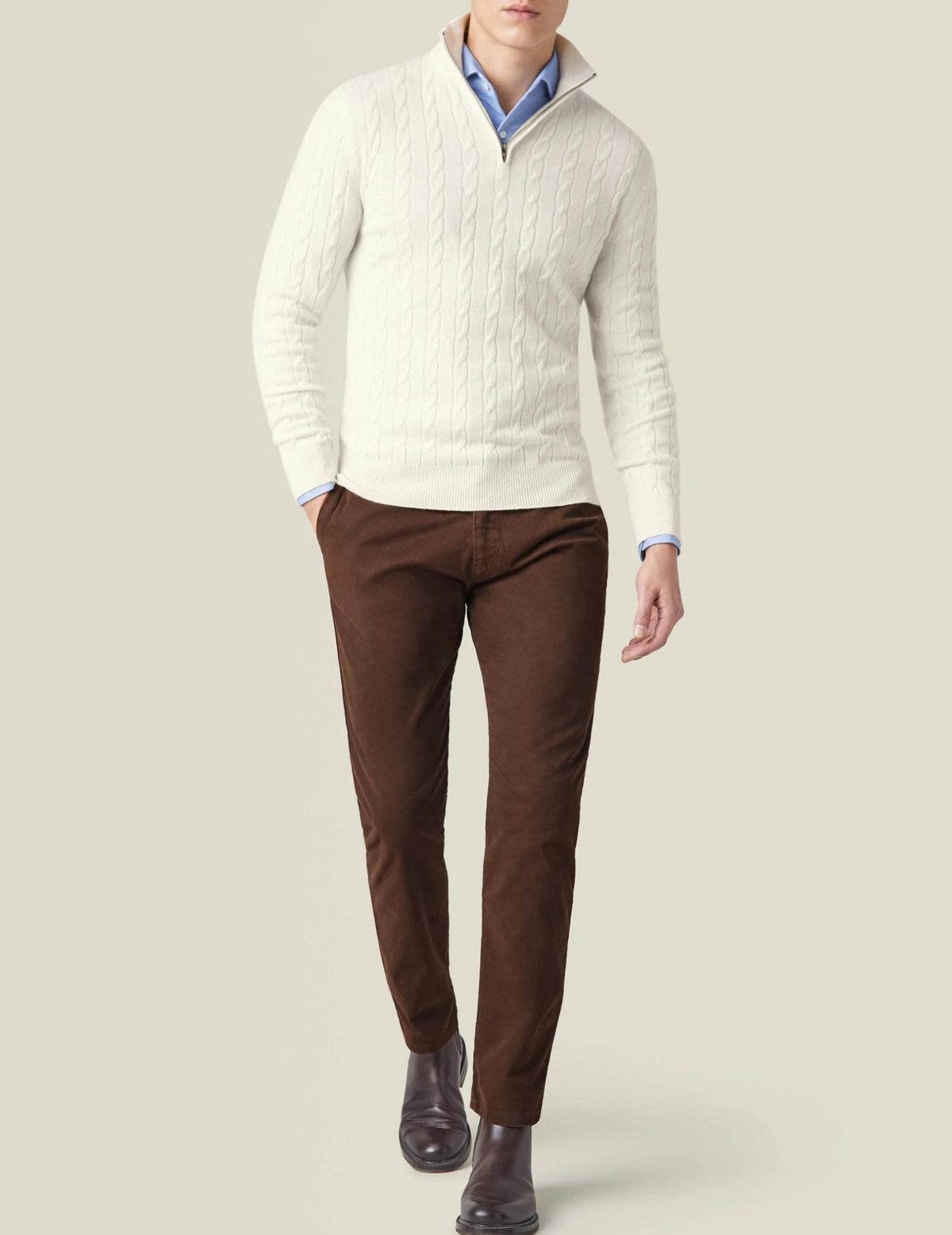 White cable knit V-neck sweater worn with a light blue collared shirt and brown pants
