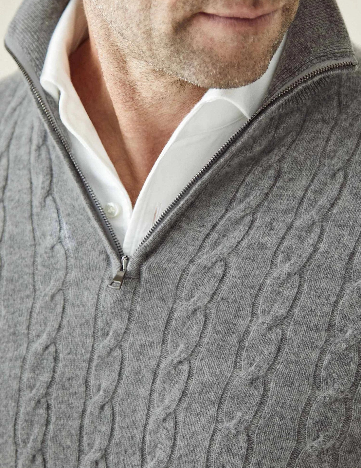 Gray cable knit V-neck sweater close-up showing textured knit pattern and white shirt collar