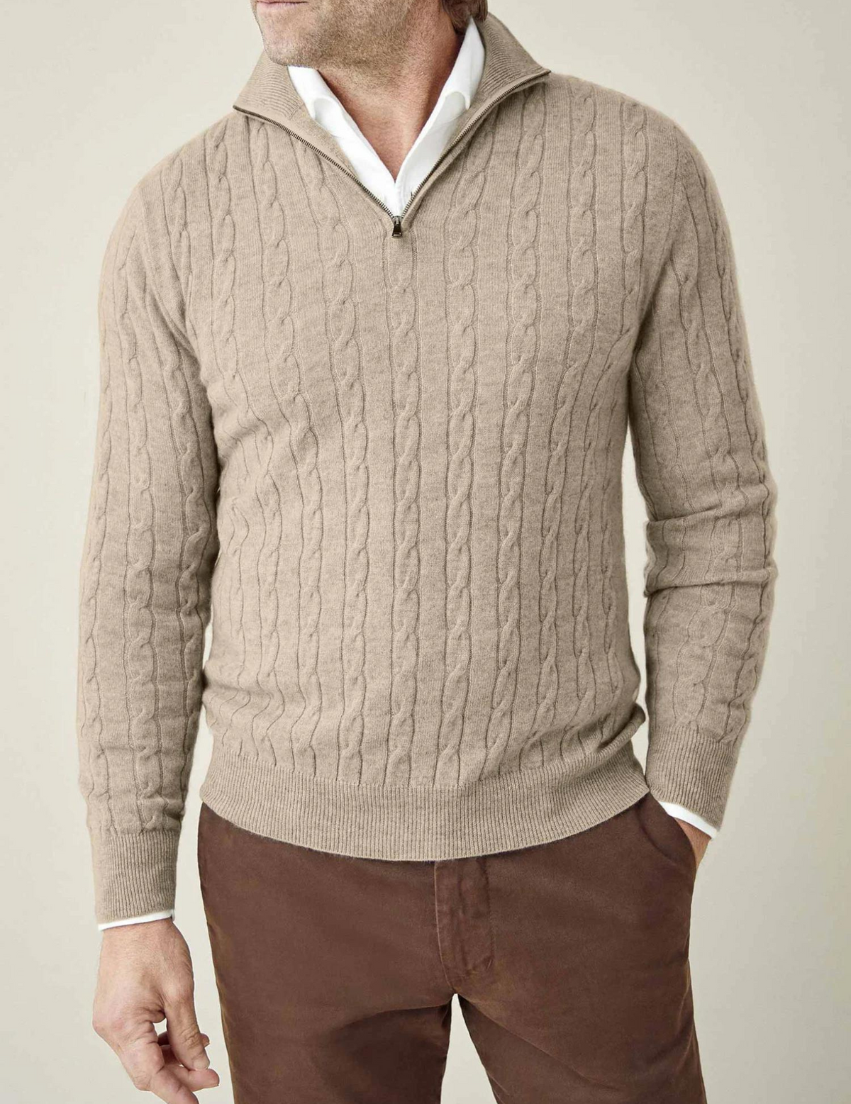 Beige cable knit V-neck sweater worn with a white collared shirt, long sleeves, and ribbed hem