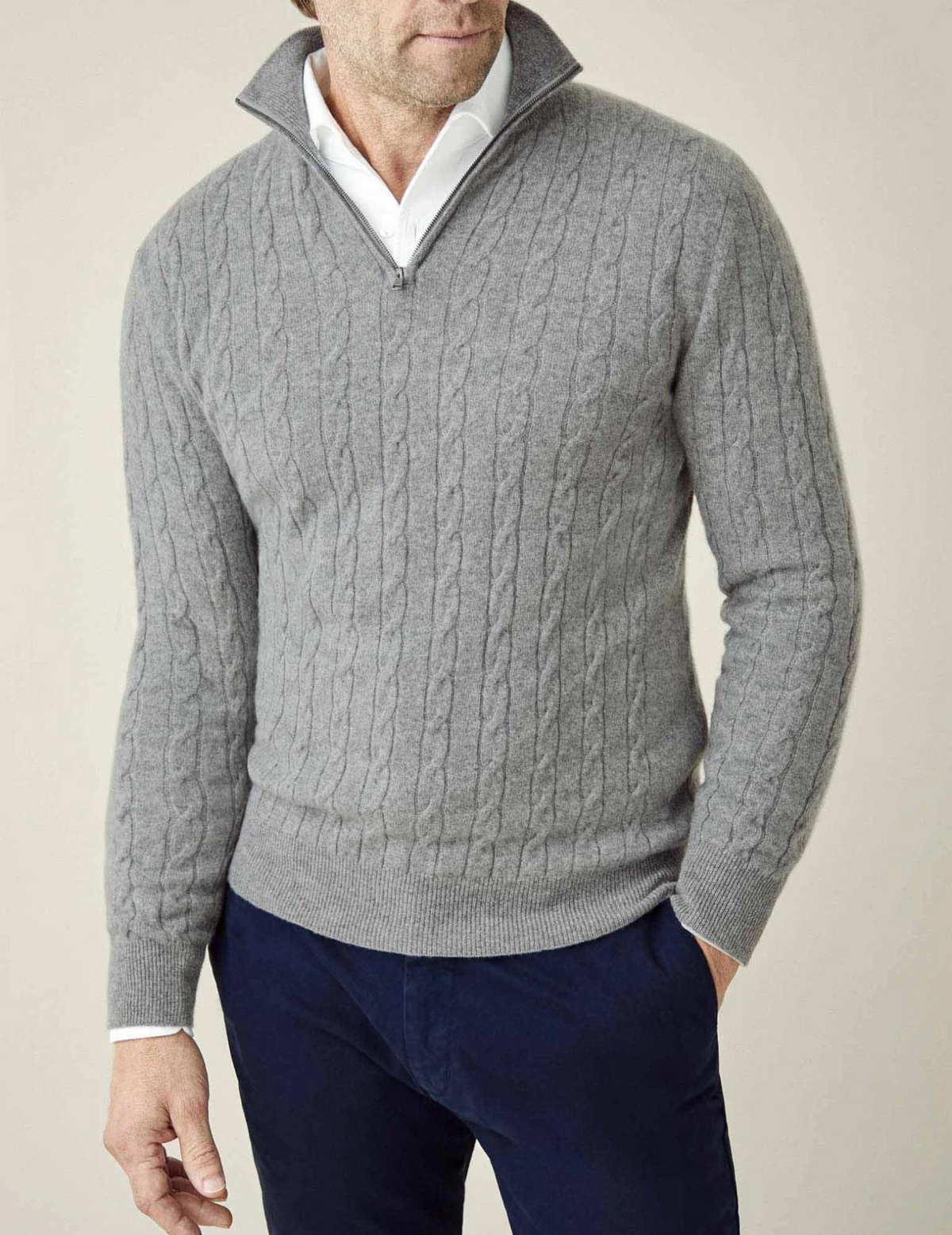Gray cable knit V-neck sweater worn with a white collared shirt, long sleeves, and ribbed hem