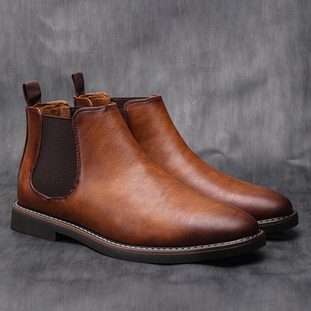 Pair of brown leather Chelsea boots with dark elastic side panels, rear pull tabs, smooth uppers, and low stacked soles.