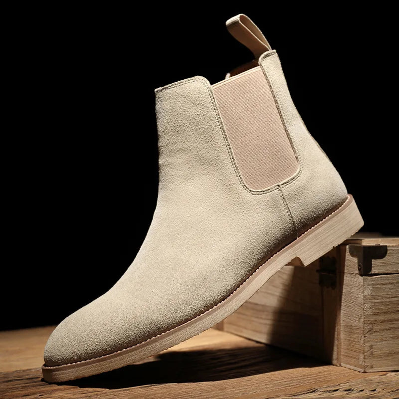 Beige Suede Chelsea boot displayed on wooden steps, highlighting the elastic side panel, pull tab, and low block heel.