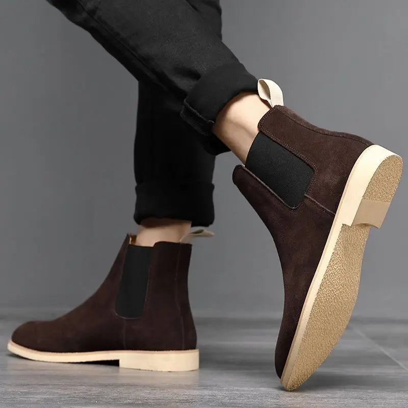 Person wearing dark brown Suede Chelsea boots while seated, showing the side profile and contrasting sole.