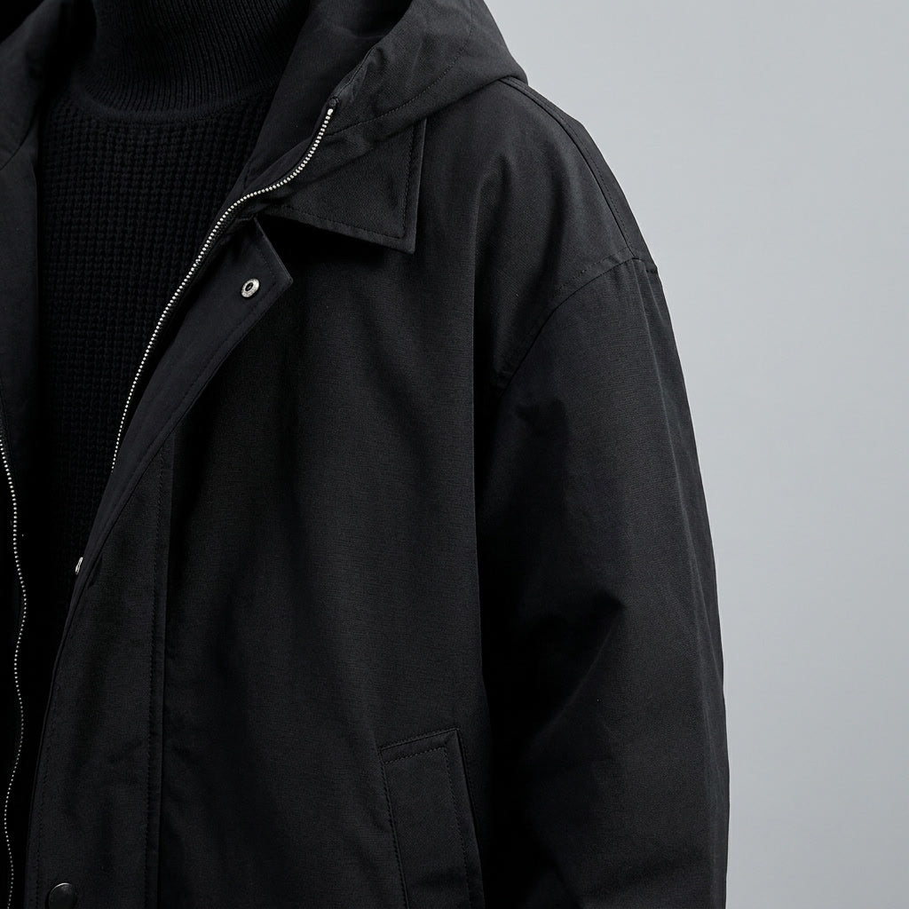 Close-up of a black hooded tailored overcoat showing the structured collar, front closure, and water-resistant shell