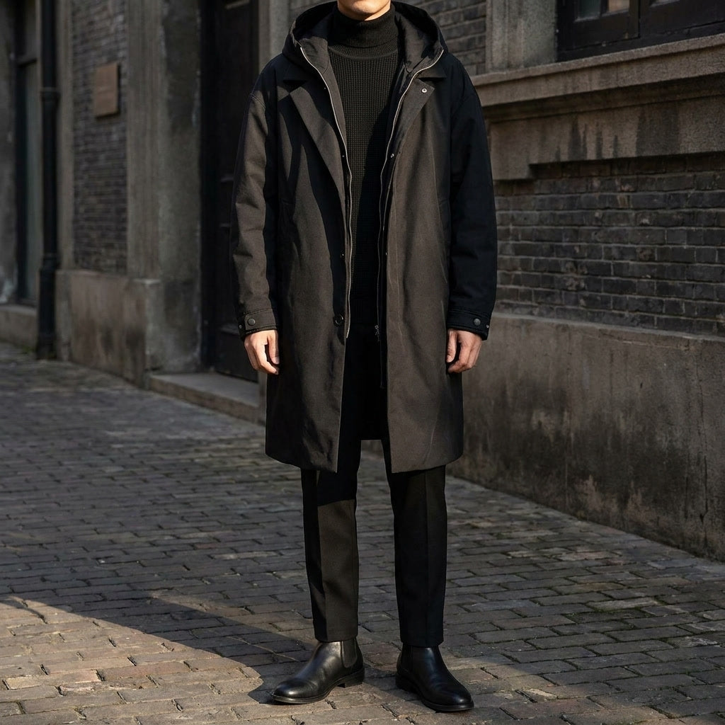 A man wearing a black hooded tailored overcoat with a water-resistant shell and longline fit, standing outdoors