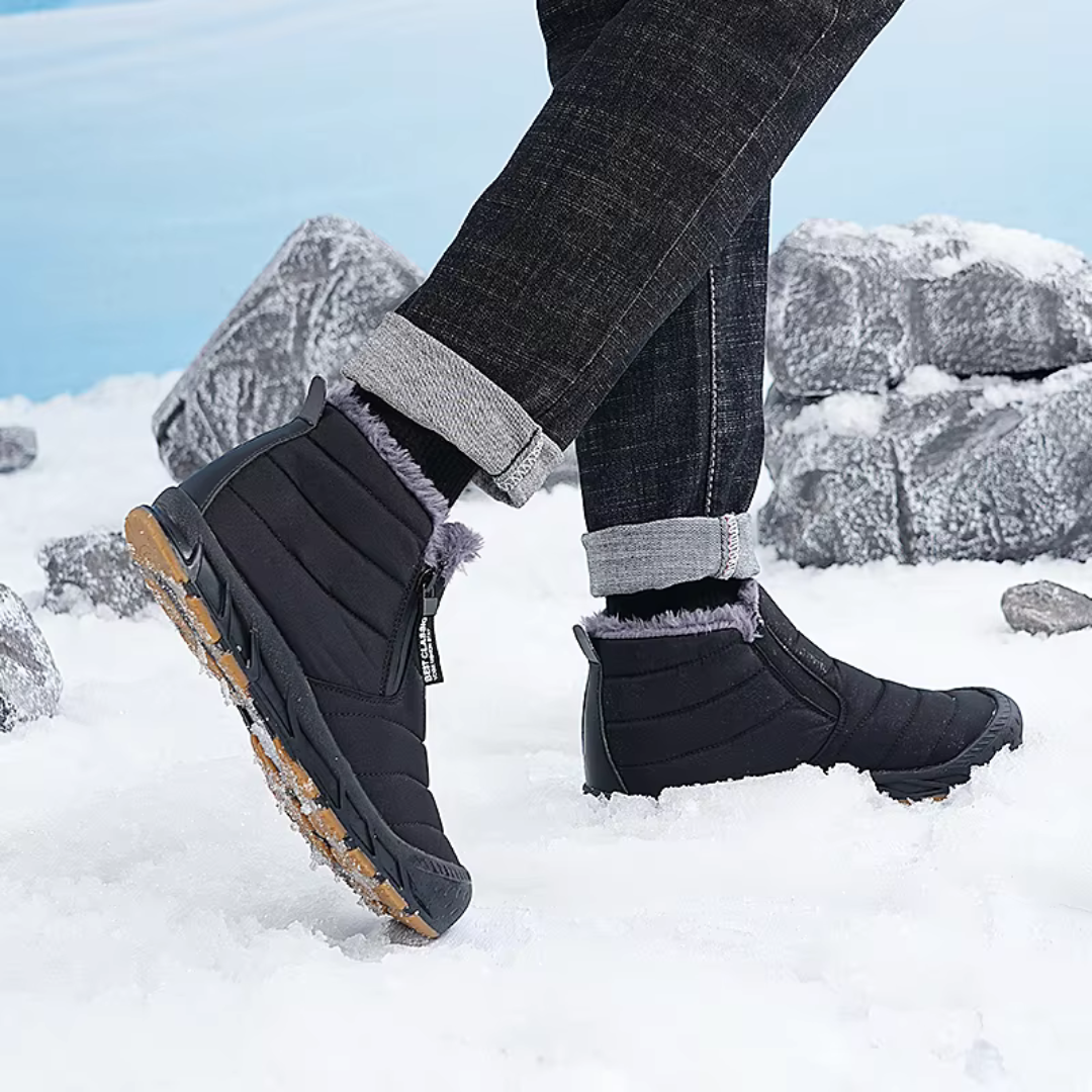 A person wearing black insulated snow boots with side zip entry and slip-resistant soles in snow