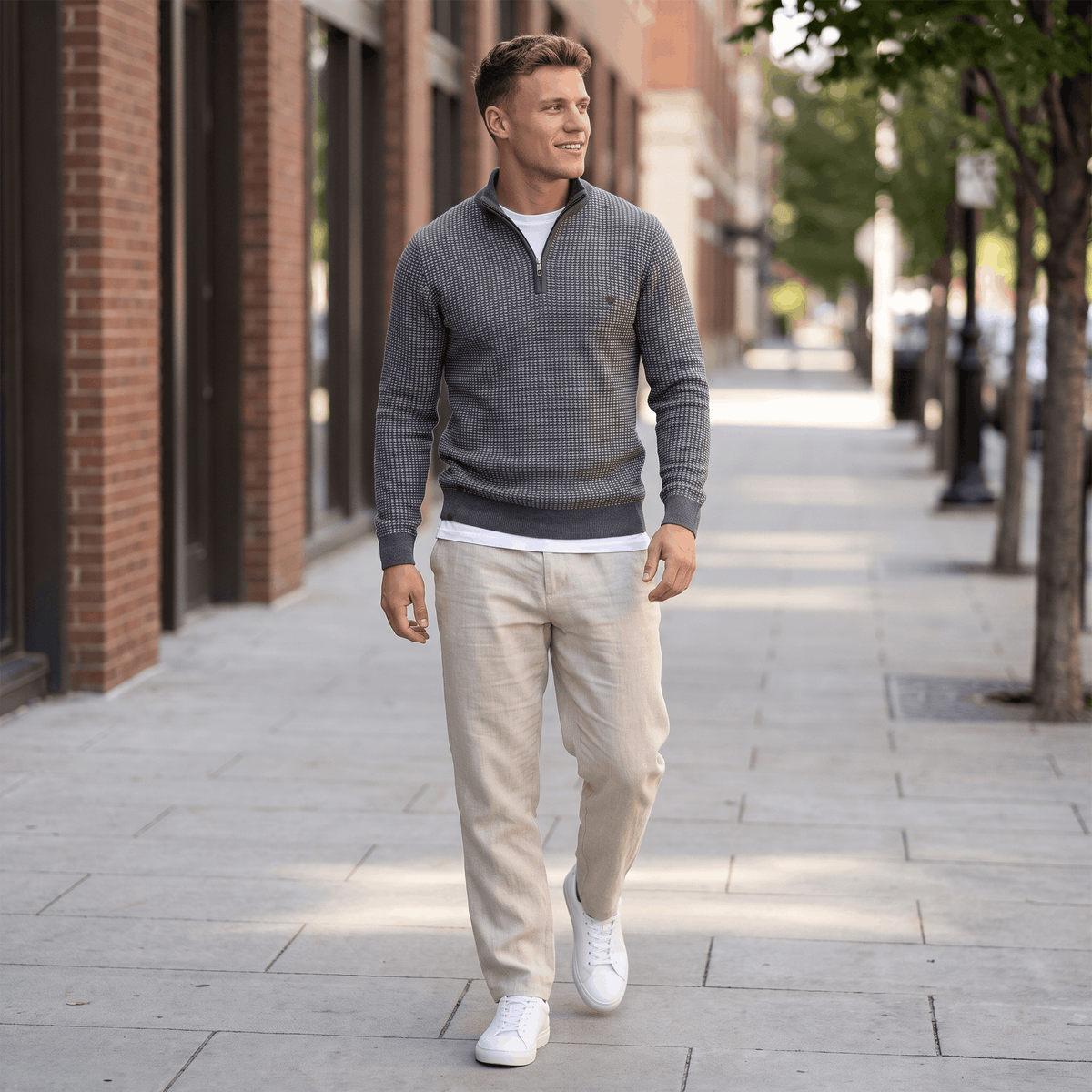 Man wearing a gray textured quarter-zip knit sweater with light-colored trousers in a casual city street setting.