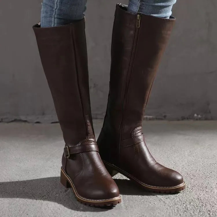 Dark brown smooth grain knee-high riding boots with a round toe, side zip, and buckled ankle strap on a low block heel.