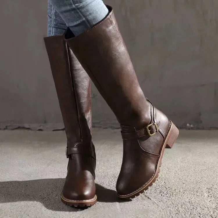 Smooth brown knee-high riding boots with a round toe, stacked block heel, and decorative ankle buckle strap.
