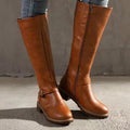 Brown smooth grain knee-high riding boots with a side zip, buckle ankle strap, and low stacked block heel.