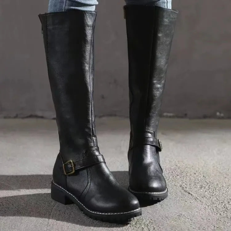 Black knee-high riding boots in smooth grain leather with a low block heel, side zip, and buckled ankle strap.