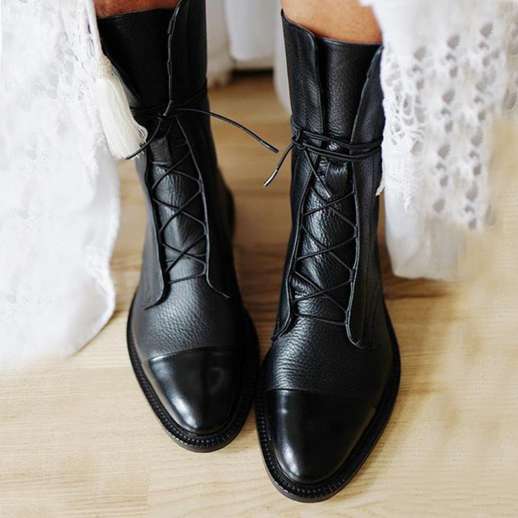 Black leather lace-up ankle boots worn with light-colored pants.
